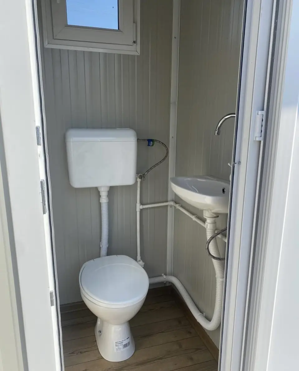 White interior of a deluxe flushing restroom unit with a toilet and small sink