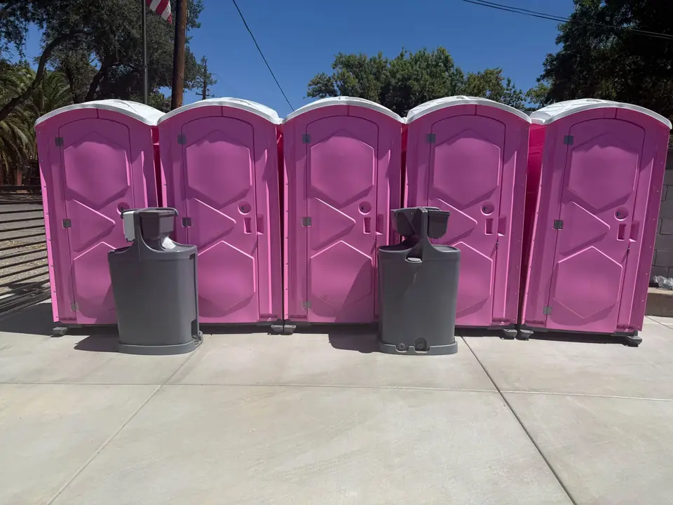 Five pink event porta potties in a row with two hand wash stations in front