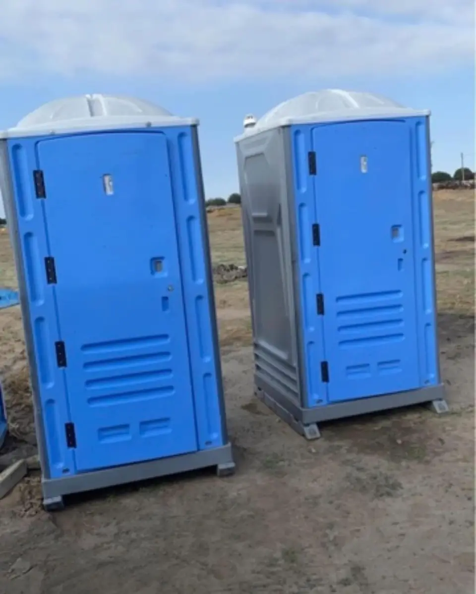 Two blue standard porta potties on a graded construction site