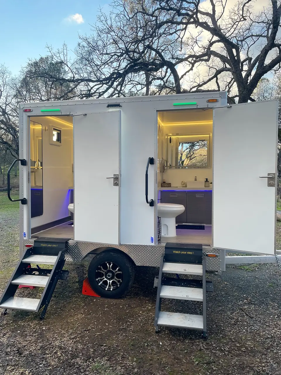 Two-stall restroom trailer with open doors, interior lights and fold-down steps